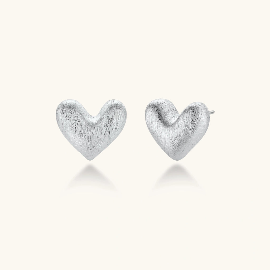 Pair of brushed platinum-plated 925 sterling silver puffy heart stud earrings on a cream background.