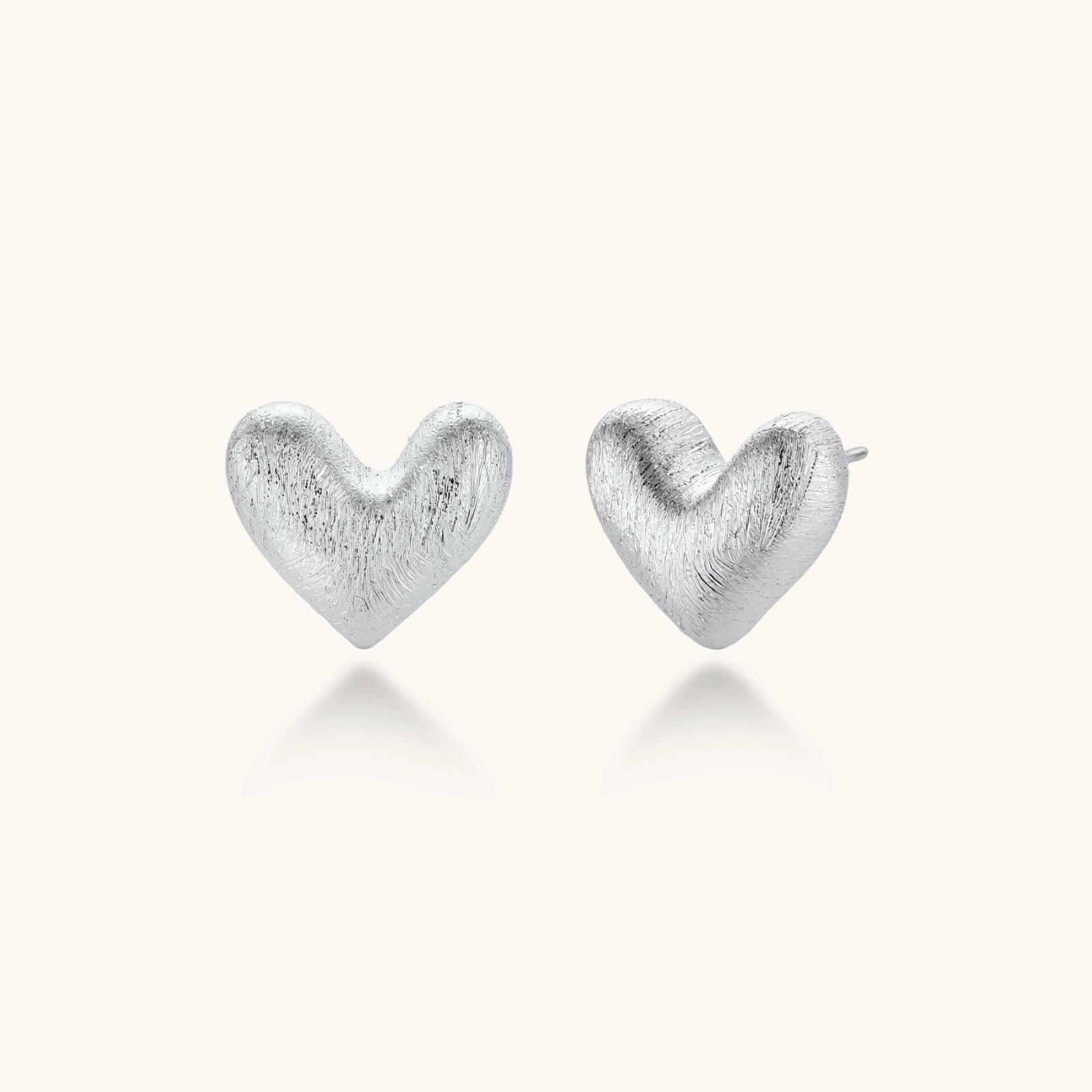 Pair of brushed platinum-plated 925 sterling silver puffy heart stud earrings on a cream background.