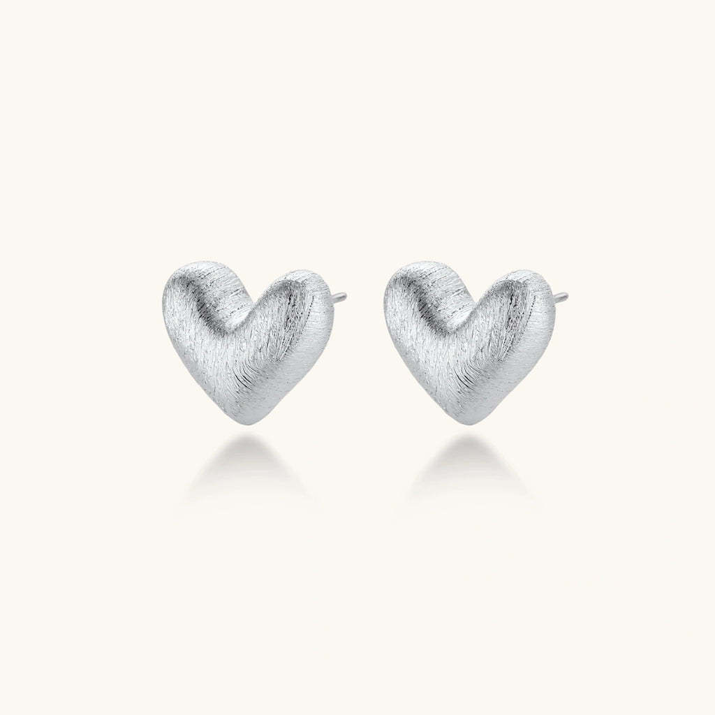 Pair of brushed platinum-plated 925 sterling silver puffy heart stud earrings on a cream background.