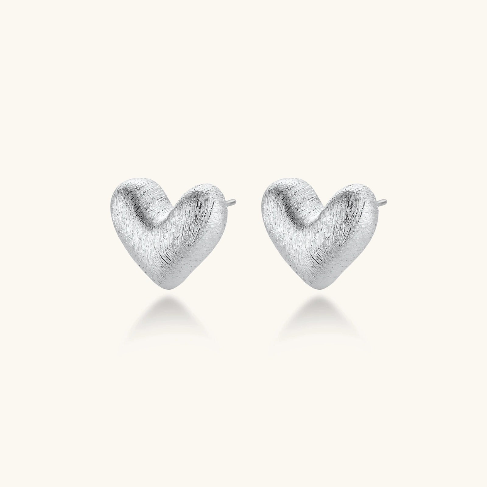 Pair of brushed platinum-plated 925 sterling silver puffy heart stud earrings on a cream background.