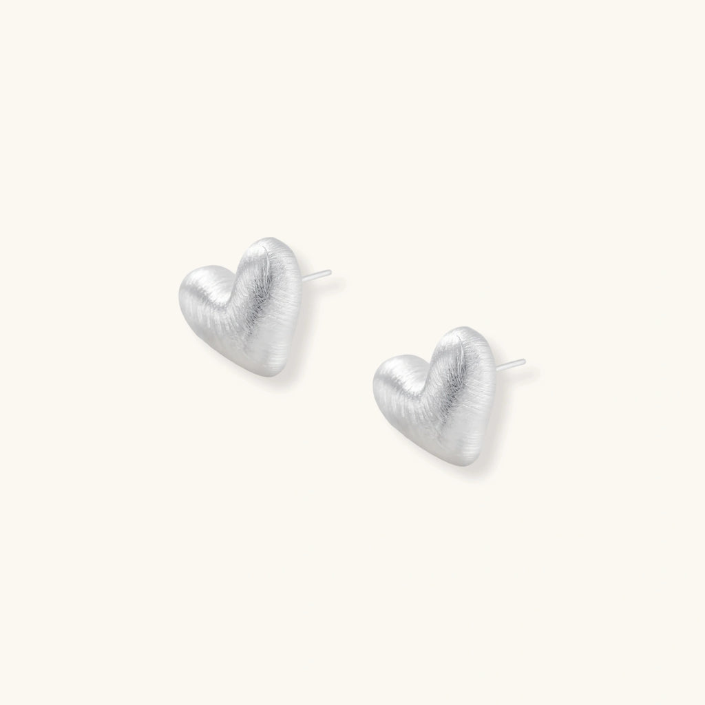 Pair of brushed platinum-plated 925 sterling silver puffy heart stud earrings on a cream background.