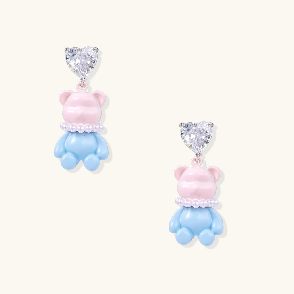 Cute pink teddy bear dangle earrings with clear crystal hearts and blue enamel details on white background.