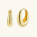 Chunky gold-plated sterling silver huggie hoop earrings with hinged closure mechanism on cream background.