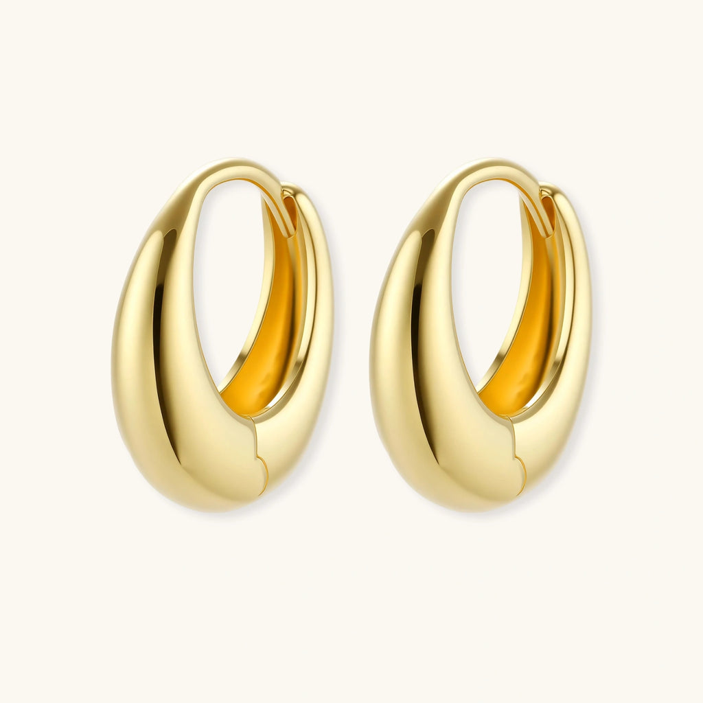 Chunky gold-plated sterling silver huggie hoop earrings with hinged closure mechanism on cream background.