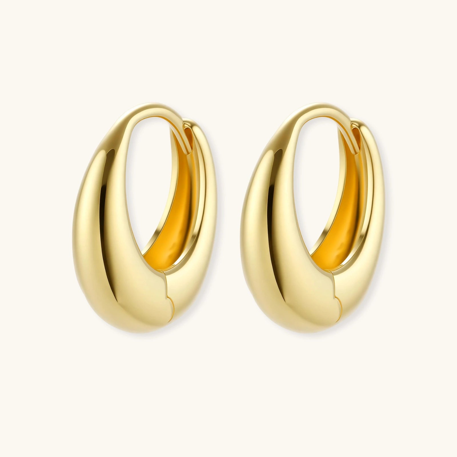 Chunky gold-plated sterling silver huggie hoop earrings with hinged closure mechanism on cream background.
