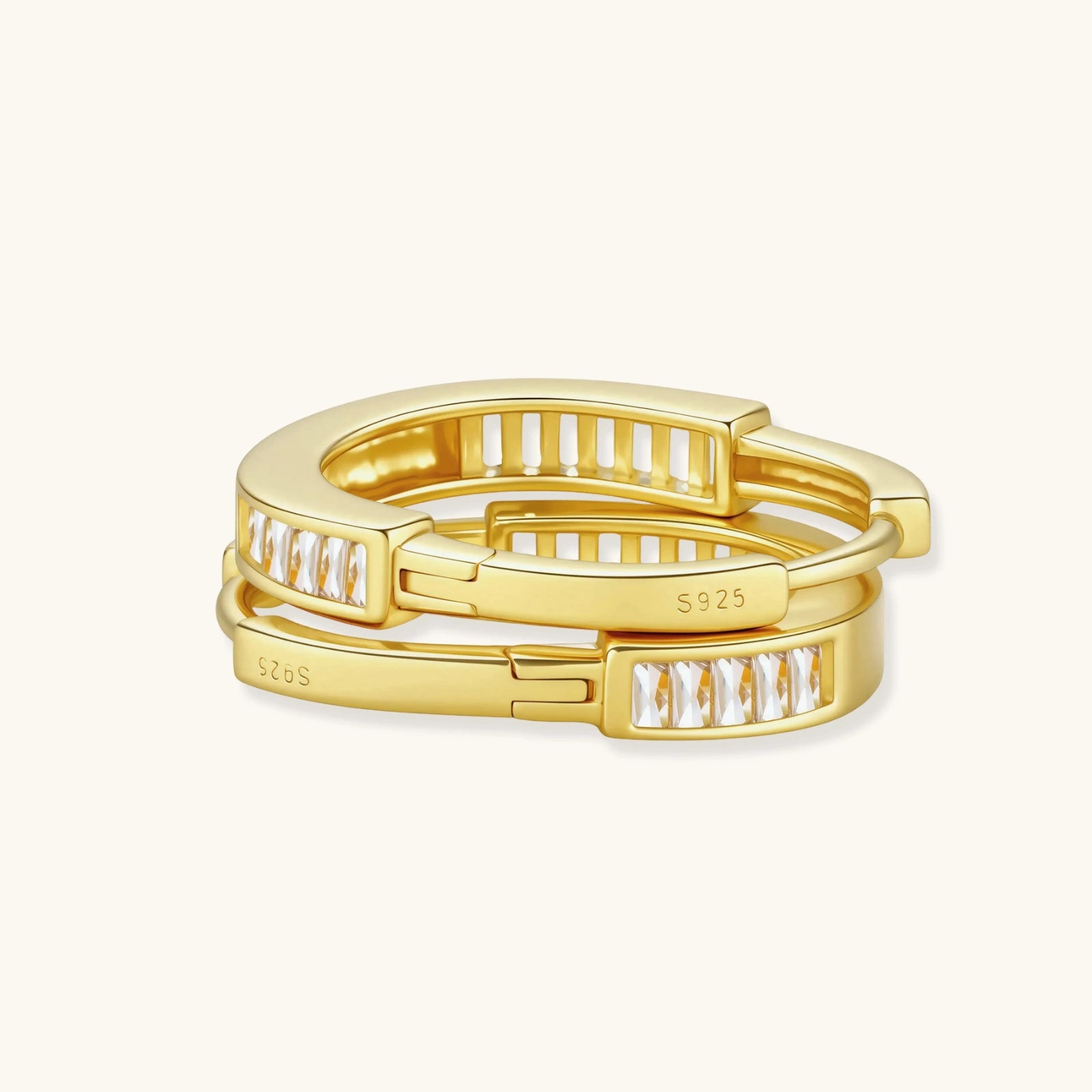 Close-up of gold-plated sterling silver huggie hoop earrings featuring rectangular cubic zirconia stones on neutral background.