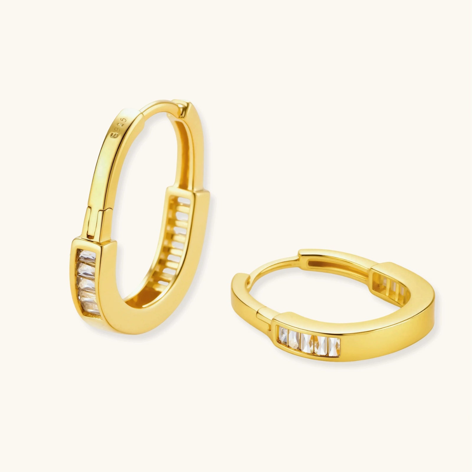 Close-up of gold-plated sterling silver huggie hoop earrings featuring rectangular cubic zirconia stones on neutral background.