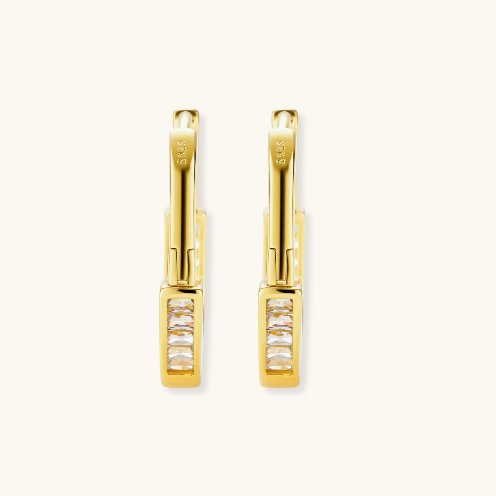 Close-up of gold-plated sterling silver huggie hoop earrings featuring rectangular cubic zirconia stones on neutral background.