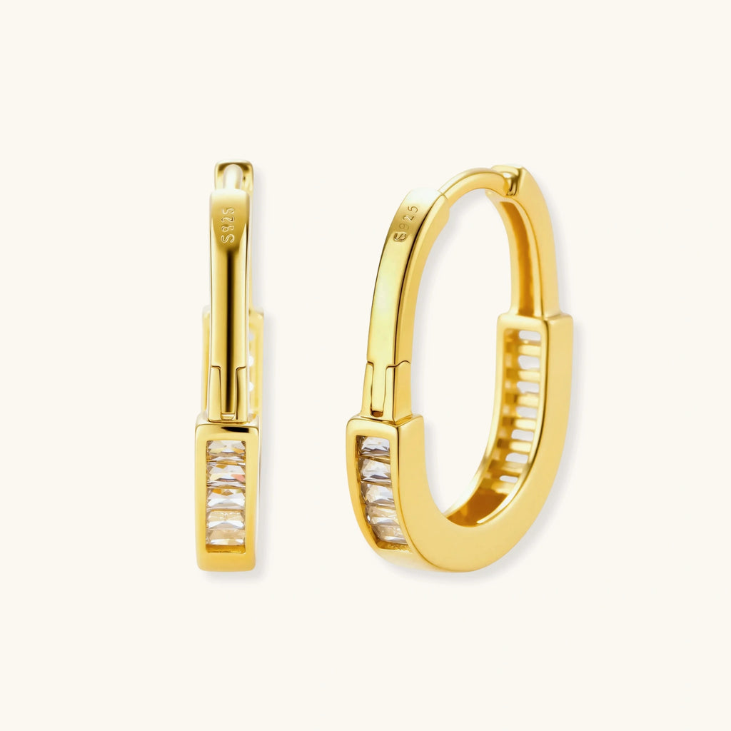 Close-up of gold-plated sterling silver huggie hoop earrings featuring rectangular cubic zirconia stones on neutral background.