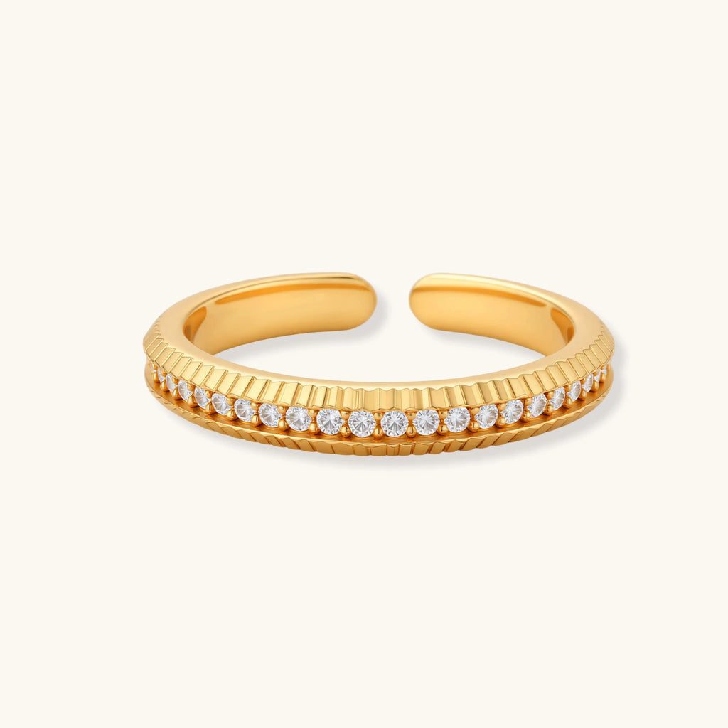Adjustable gold-plated ring with row of sparkling crystals on ribbed band, shot against cream background
