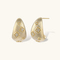 Curved gold-plated hoop earrings with four-leaf clover and diamond-shaped crystal details on white background