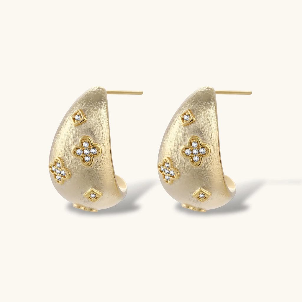 Curved gold-plated hoop earrings with four-leaf clover and diamond-shaped crystal details on white background