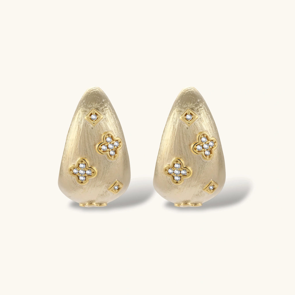 Curved gold-plated hoop earrings with four-leaf clover and diamond-shaped crystal details on white background