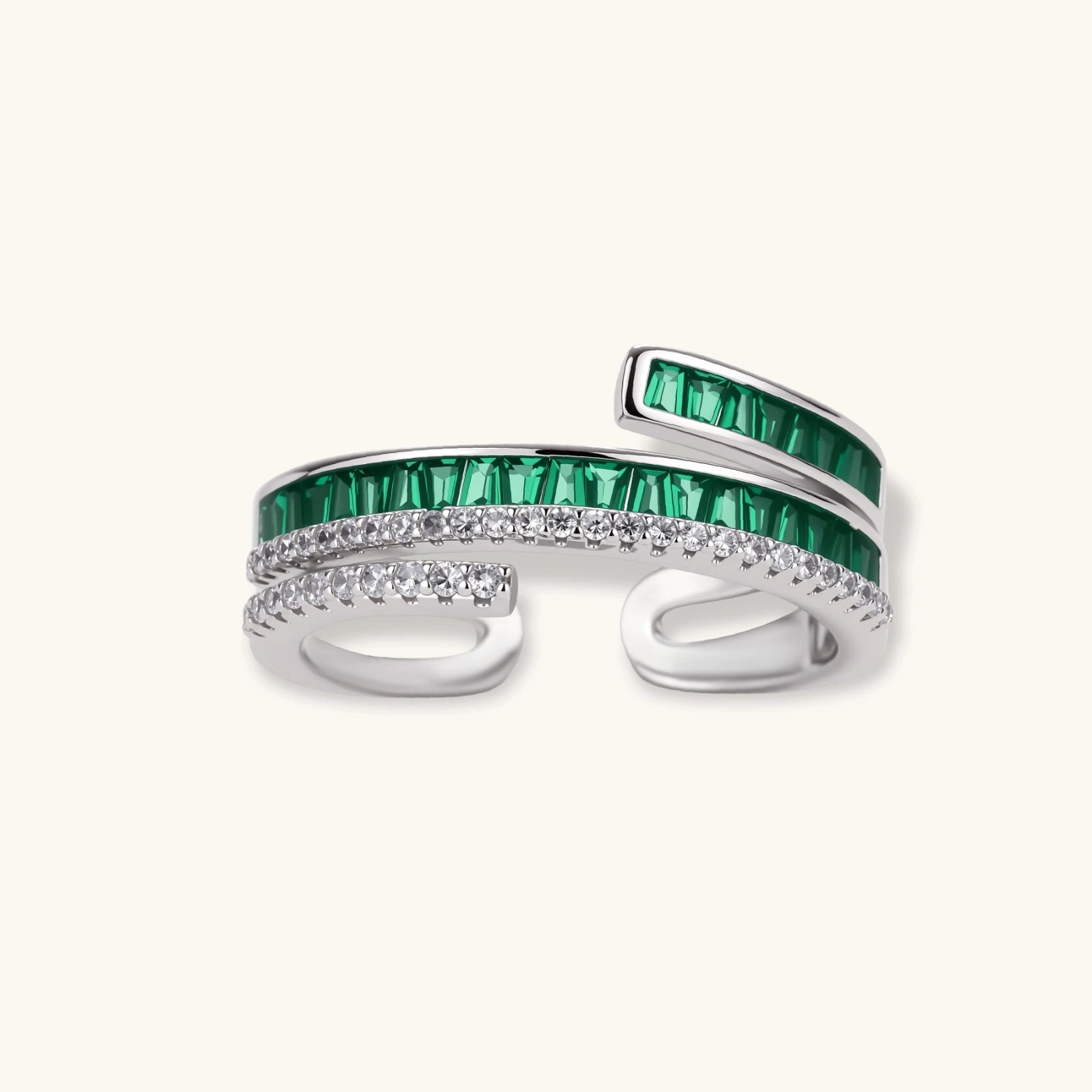 Modern adjustable ring with green baguette stones and clear crystals in parallel bands on white background.