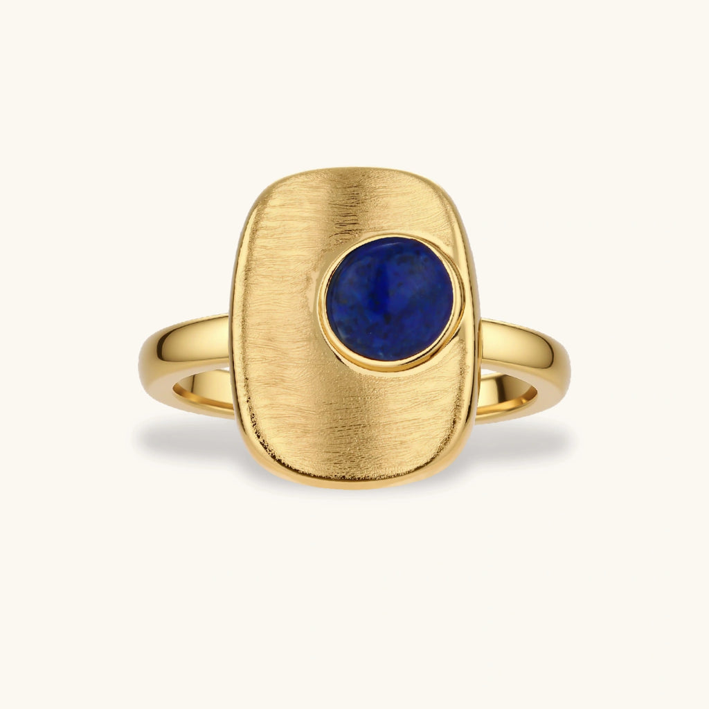 Adjustable gold-plated ring with textured square setting featuring a round blue lapis lazuli stone on cream background.