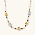 Gold-plated beaded necklace with iridescent baroque pearls, turquoise stones, and brown natural beads on neutral background.