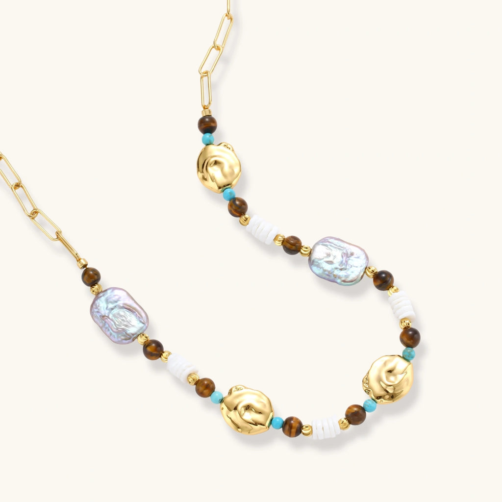 Gold-plated beaded necklace with iridescent baroque pearls, turquoise stones, and brown natural beads on neutral background.