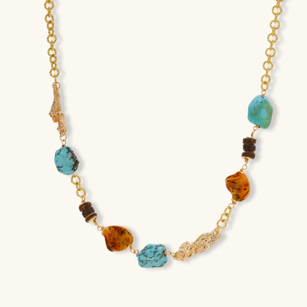 Statement necklace with gold chain, turquoise stones, amber beads, and wooden elements on cream background.