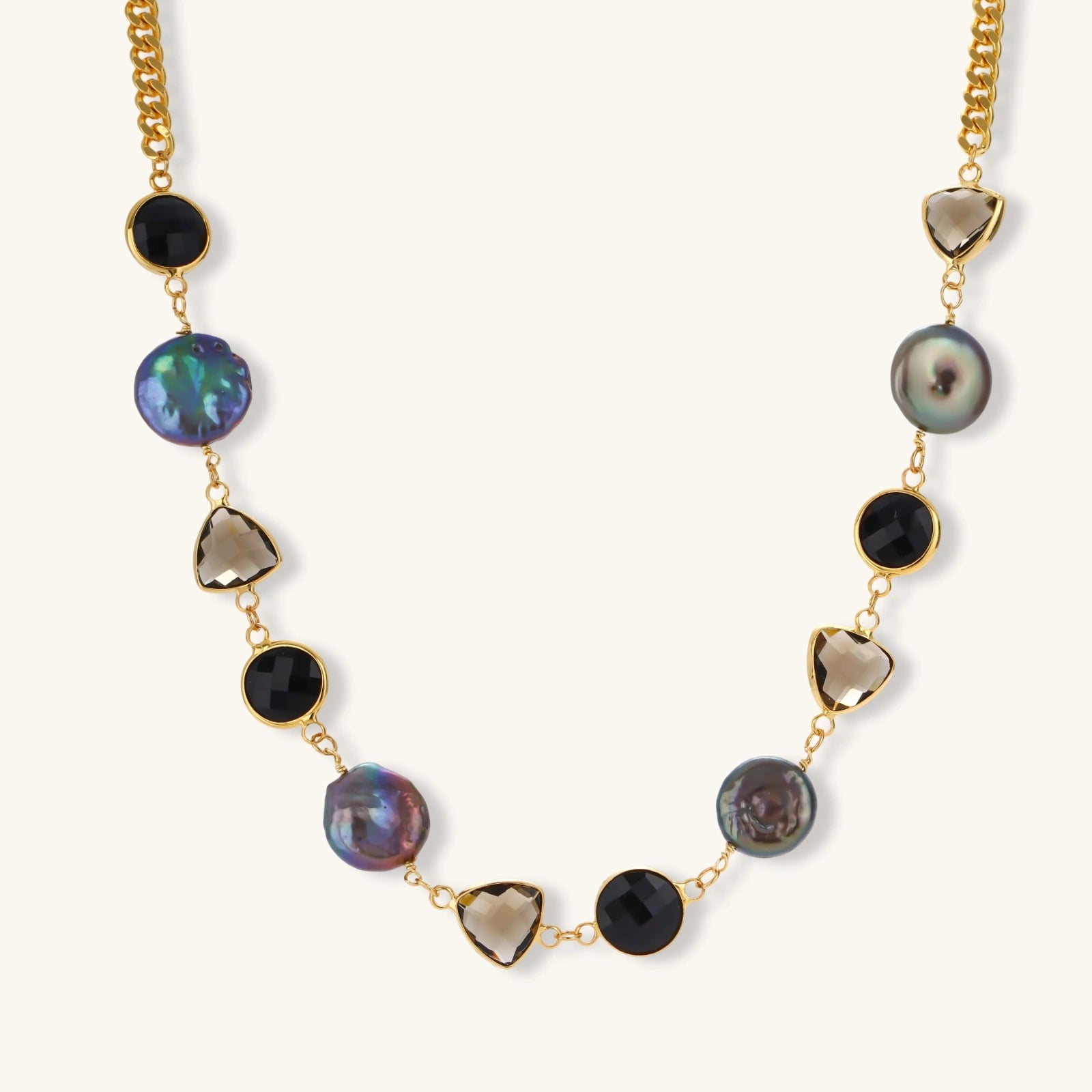 18k gold-plated chain necklace featuring lustrous baroque pearls, black onyx rounds, and smoky quartz triangular stones on white background.