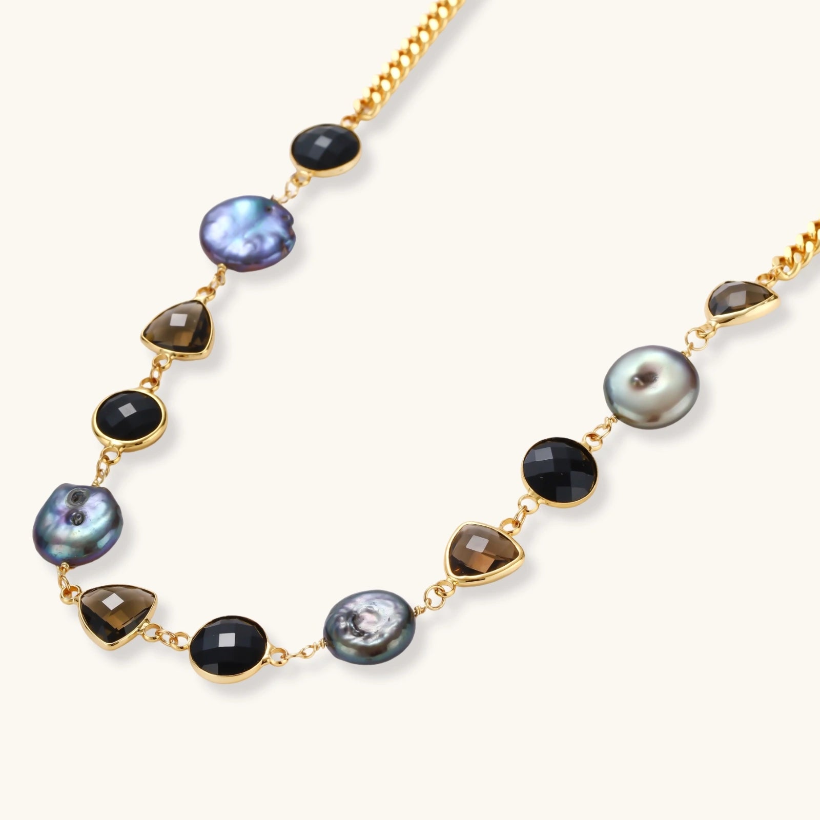 18k gold-plated chain necklace featuring lustrous baroque pearls, black onyx rounds, and smoky quartz triangular stones on white background.
