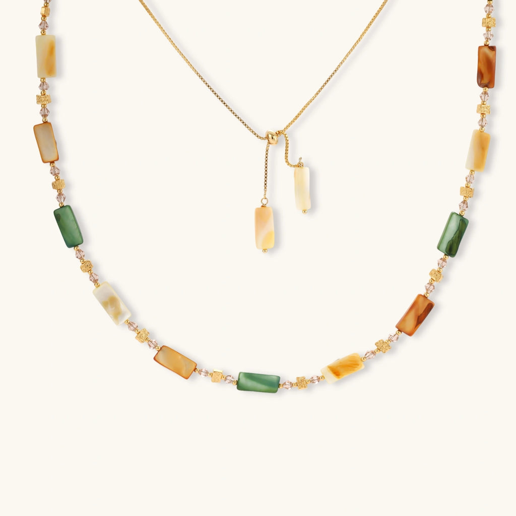 Adjustable gold-plated necklace with natural shell beads in green, amber, and cream tones on neutral background.