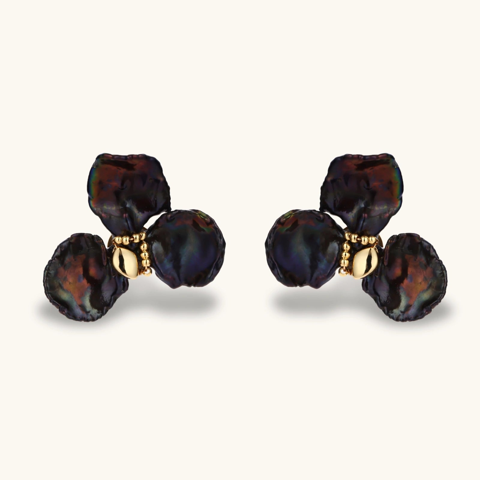 Dark iridescent baroque pearls arranged in flower pattern with 18K gold-plated center on cream background.