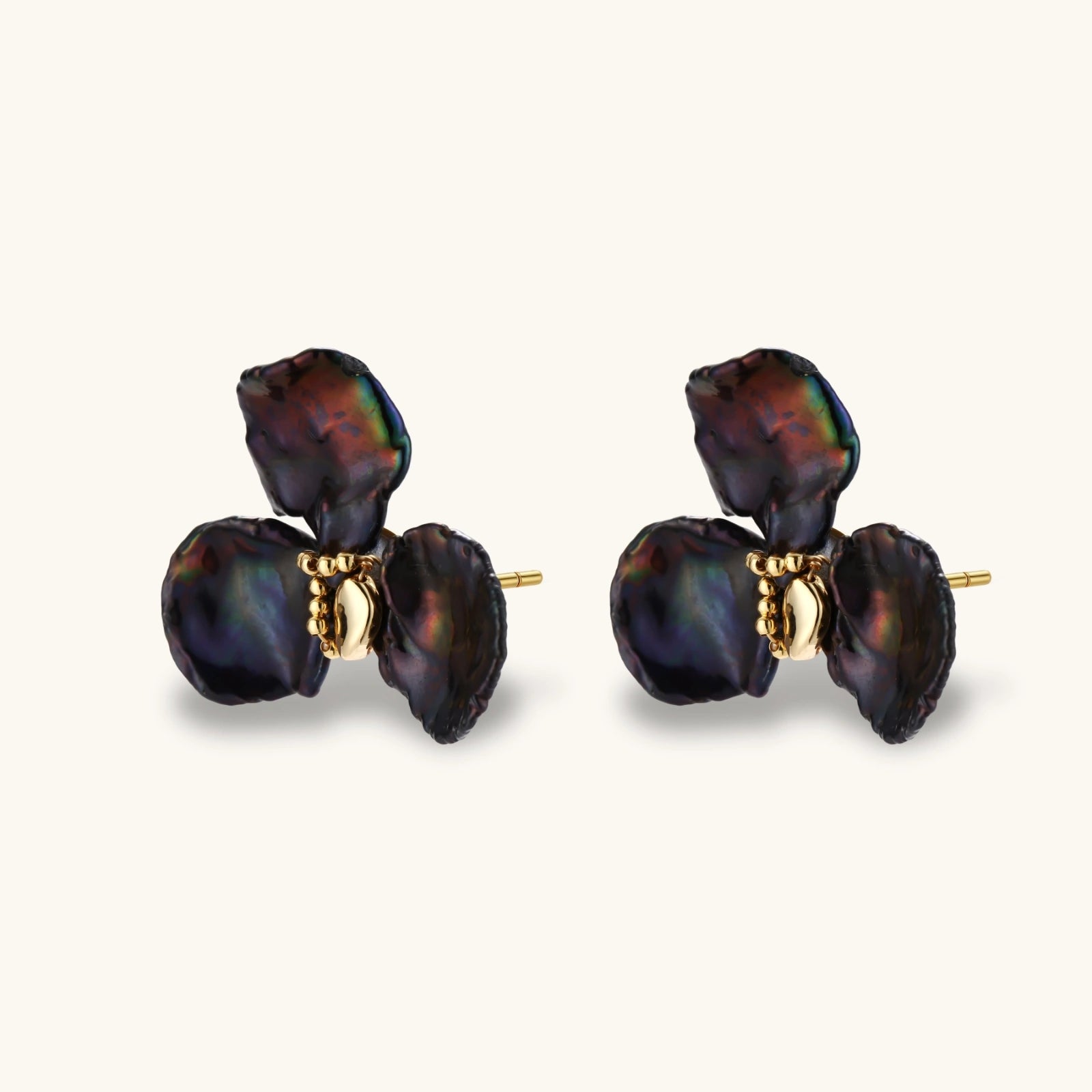 Dark iridescent baroque pearls arranged in flower pattern with 18K gold-plated center on cream background.