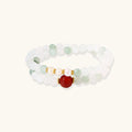 Three layered white beaded bracelets with carved orange agate lotus centerpiece and freshwater pearls on cream background.